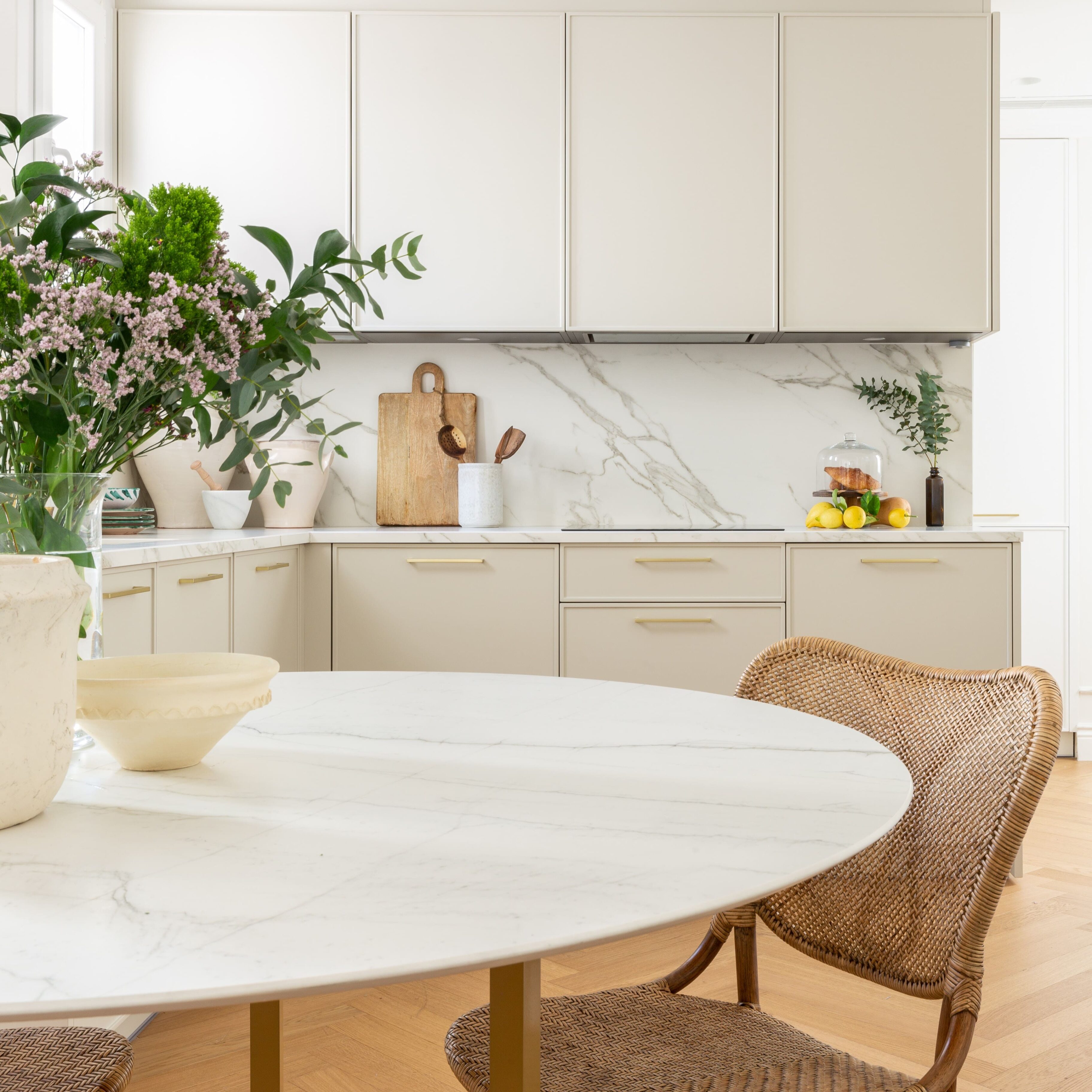 Cocina moderna con muebles beige y mesón de mármol blanco. Detalles de plantas y decoración.
