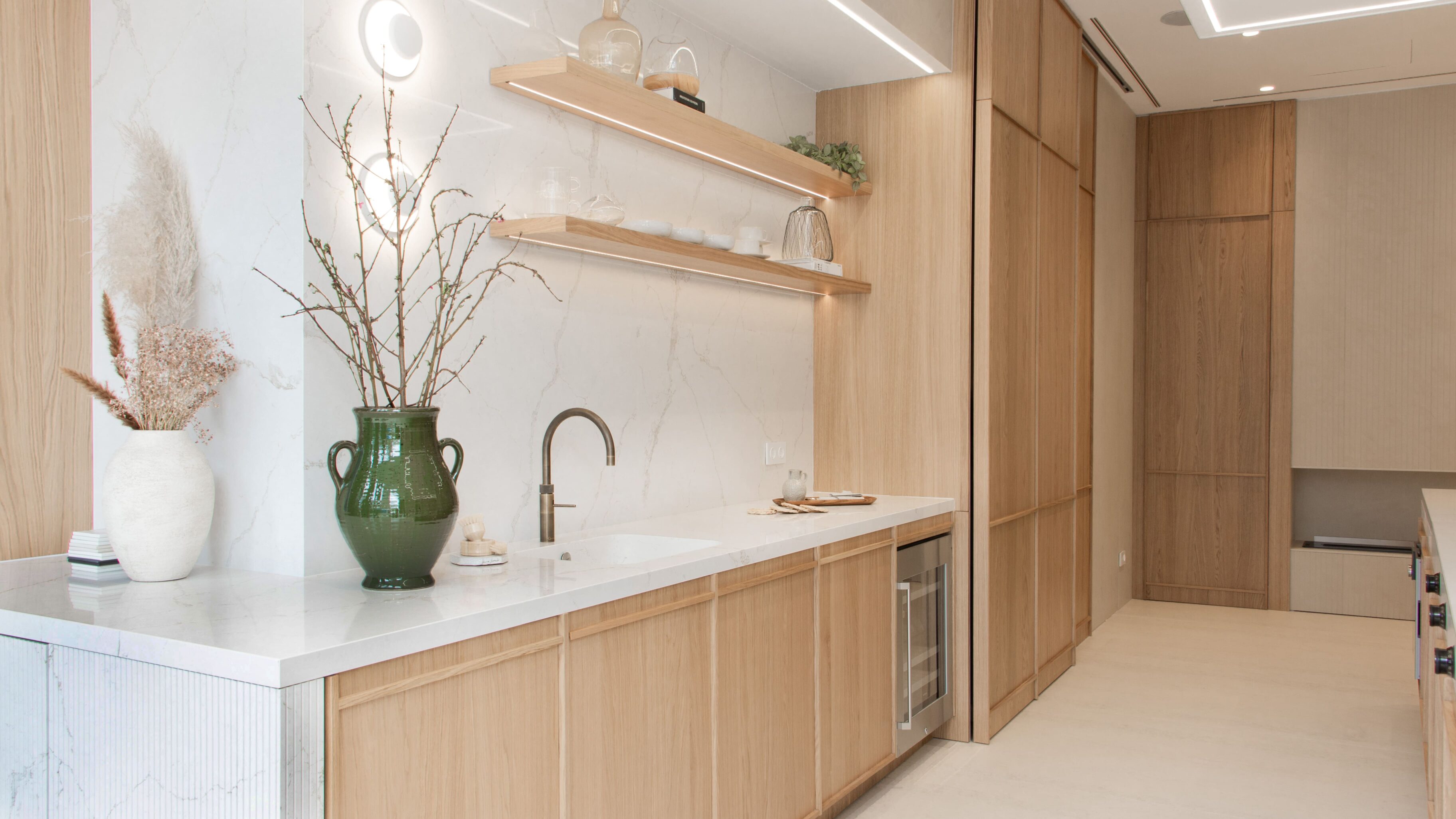 Cocina con muebles de madera clara, encimera blanca y decoración minimalista