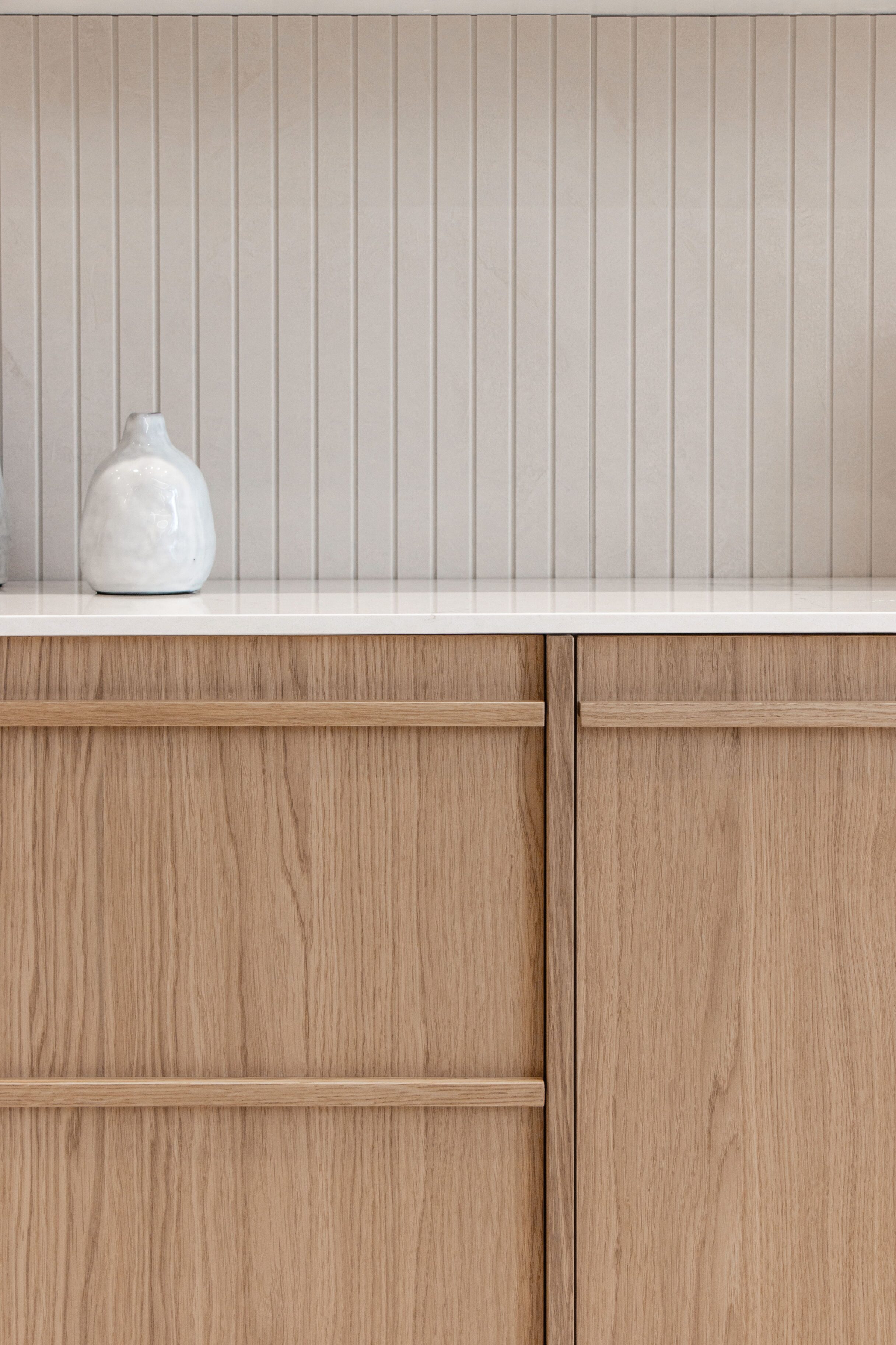 Muebles de cocina en color madera con tiradores integrados y encimera blanca.