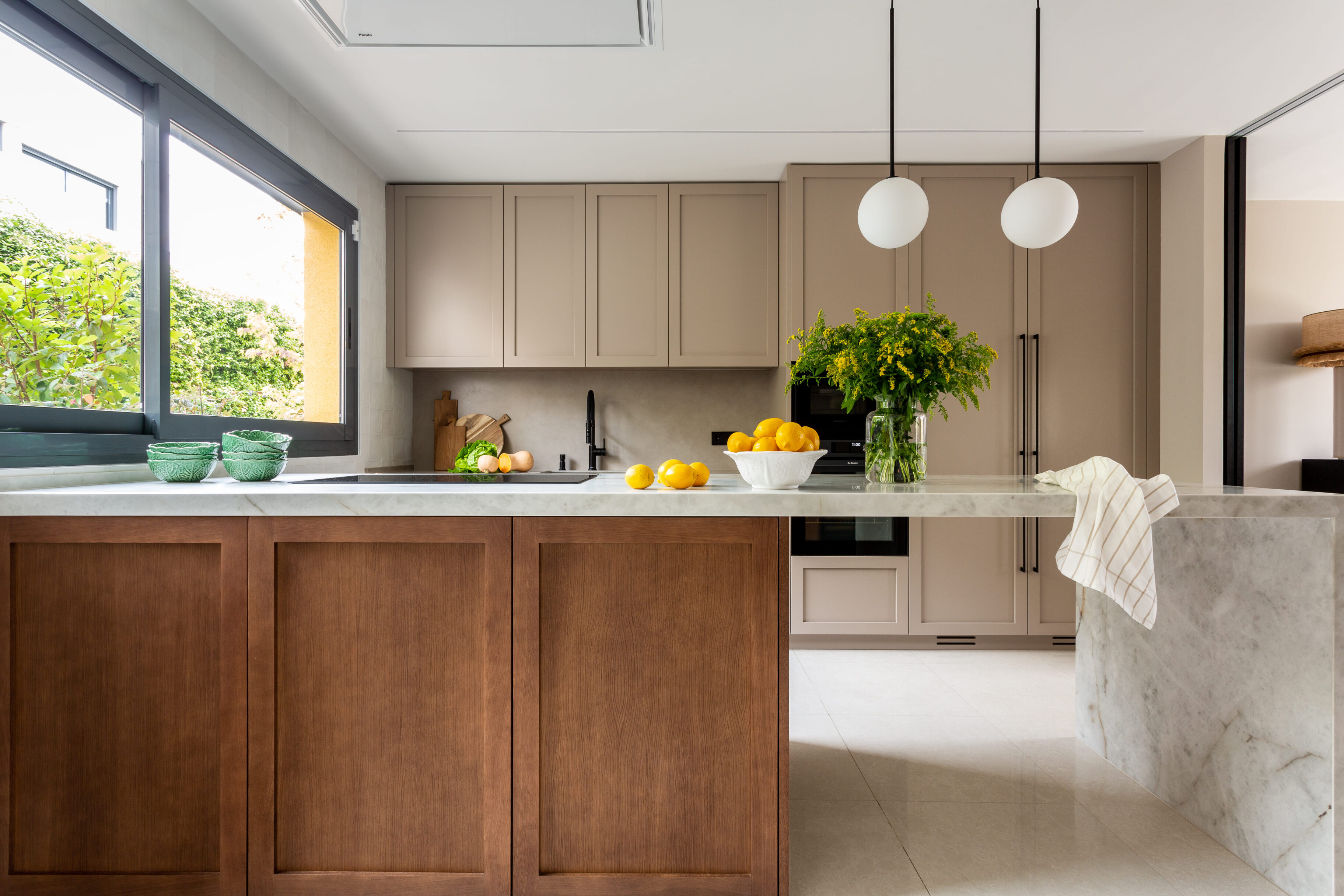 Cocina contemporánea con isla de mármol, muebles en tonos beige y madera, decorada con frutas.