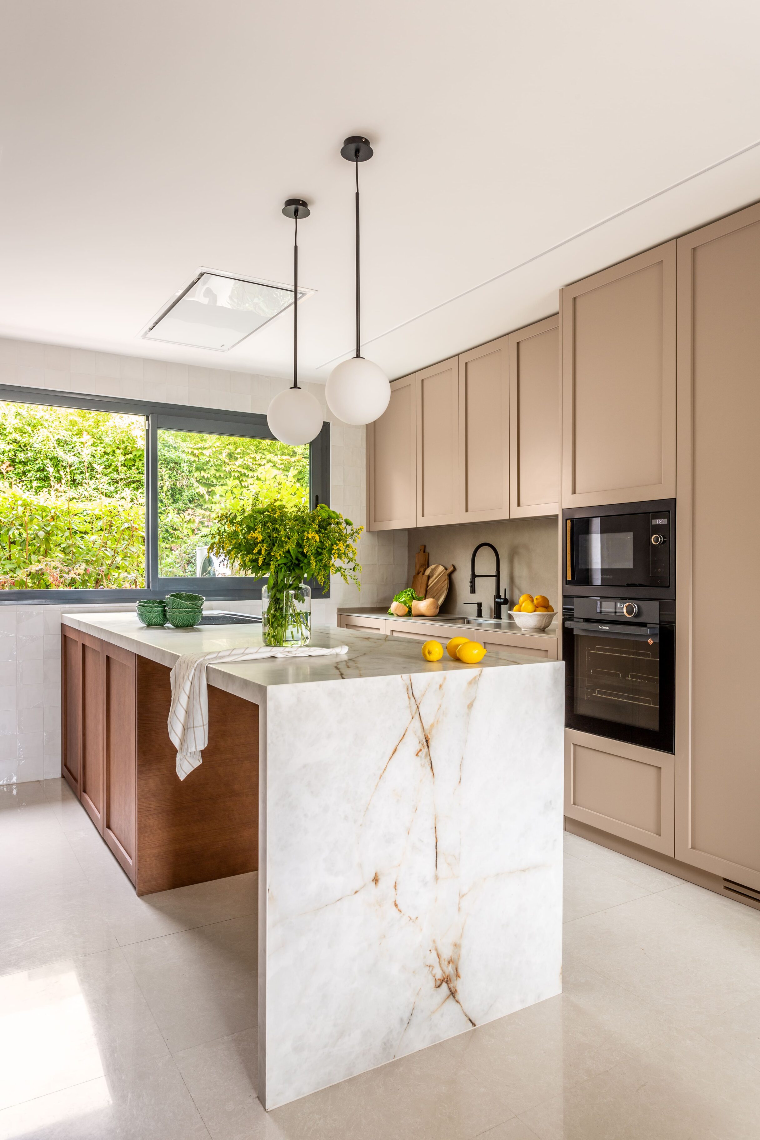 Cocina con isla de mármol blanco y armarios en tonos claros, decorada con flores y frutas