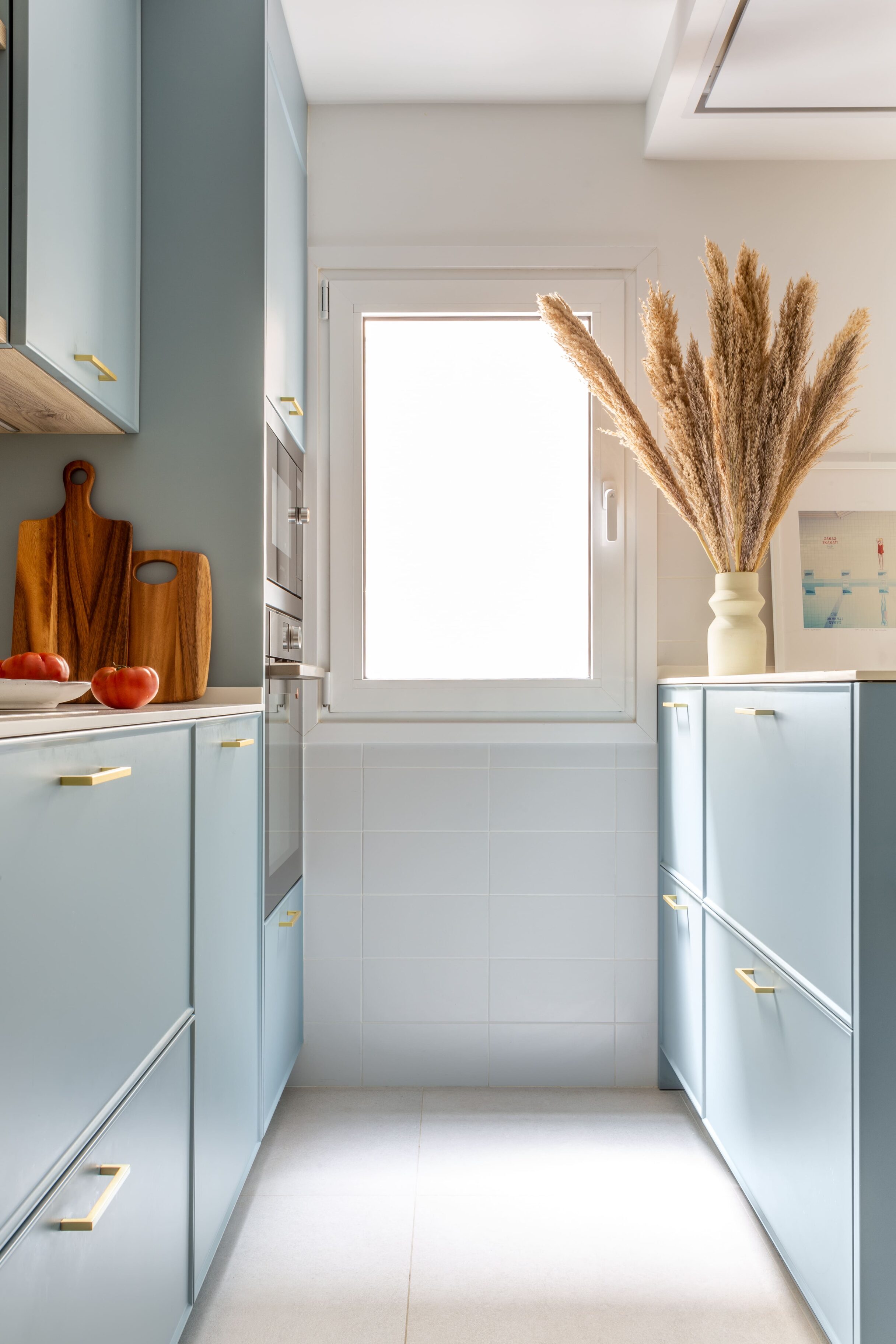 Cocina con muebles de color azul, encimera clara y decoración con flores secas.