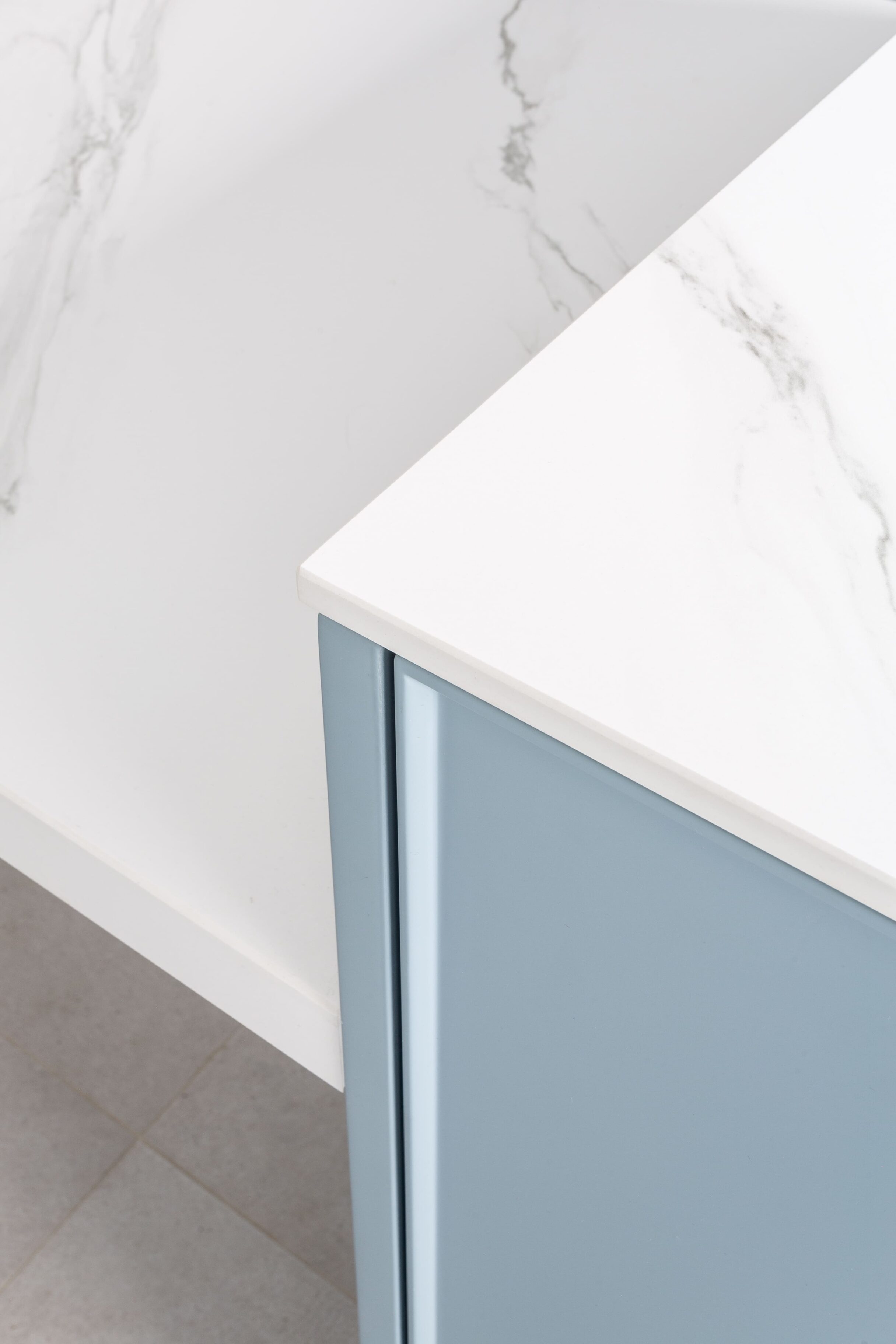 Encimera blanca con vetas grises y mueble de cocina azul claro en el borde inferior.