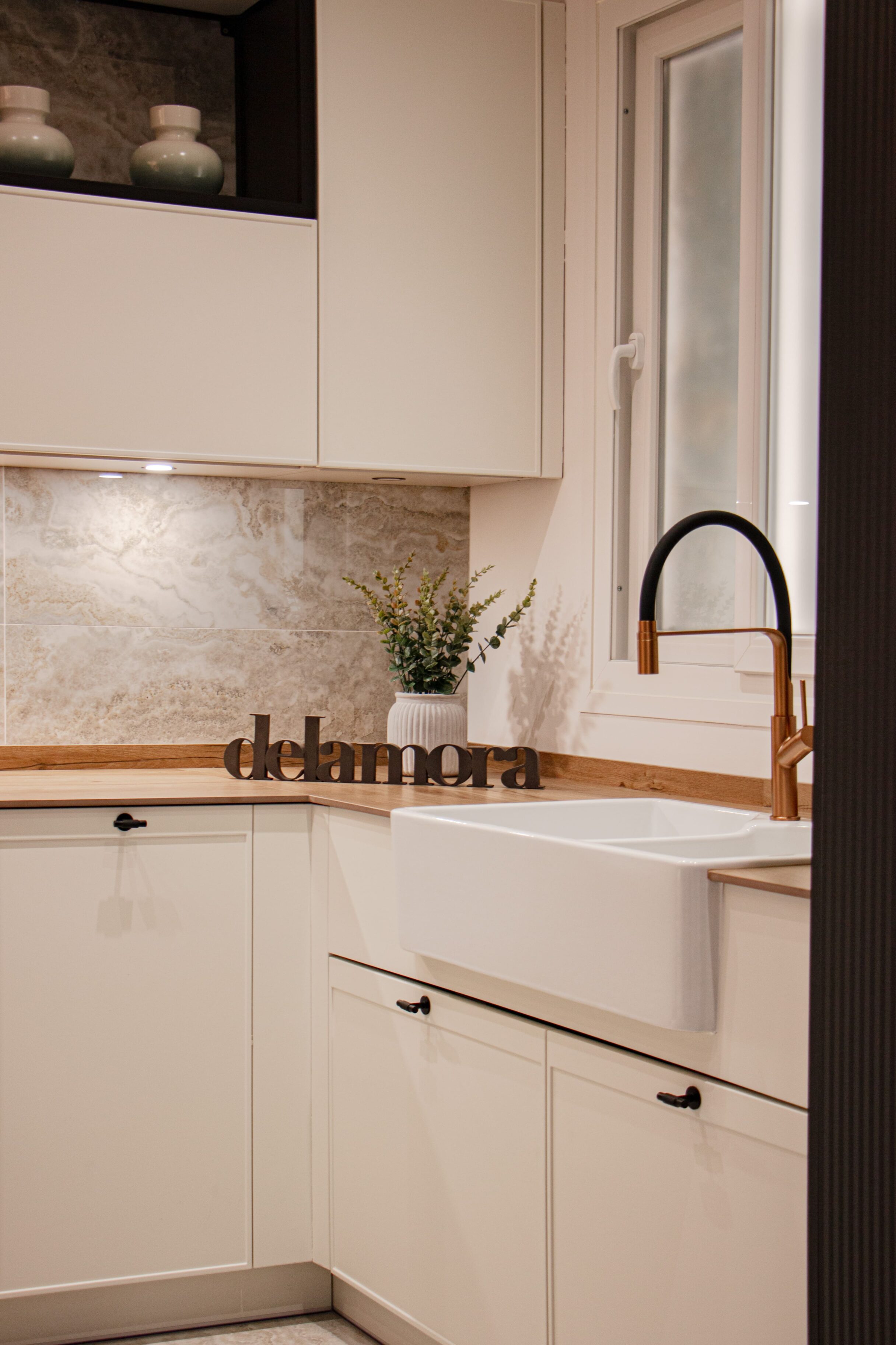 Cocina con muebles blancos, grifo negro y lavabo blanco de cerámica, mostrador de madera y decoración simple