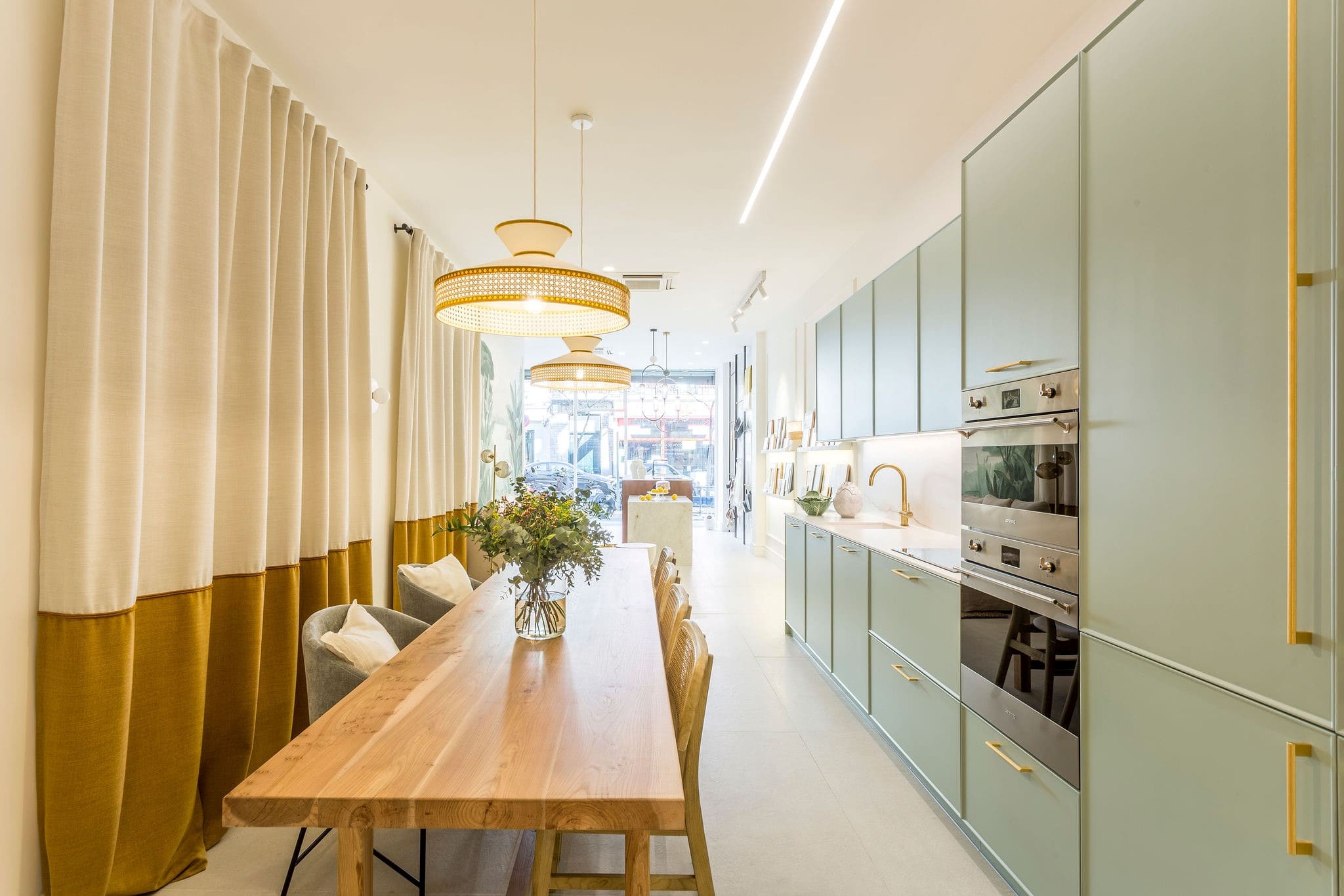 Cocina contemporánea con muebles en color azul claro y detalles en dorado, iluminación técnica y mesa de madera