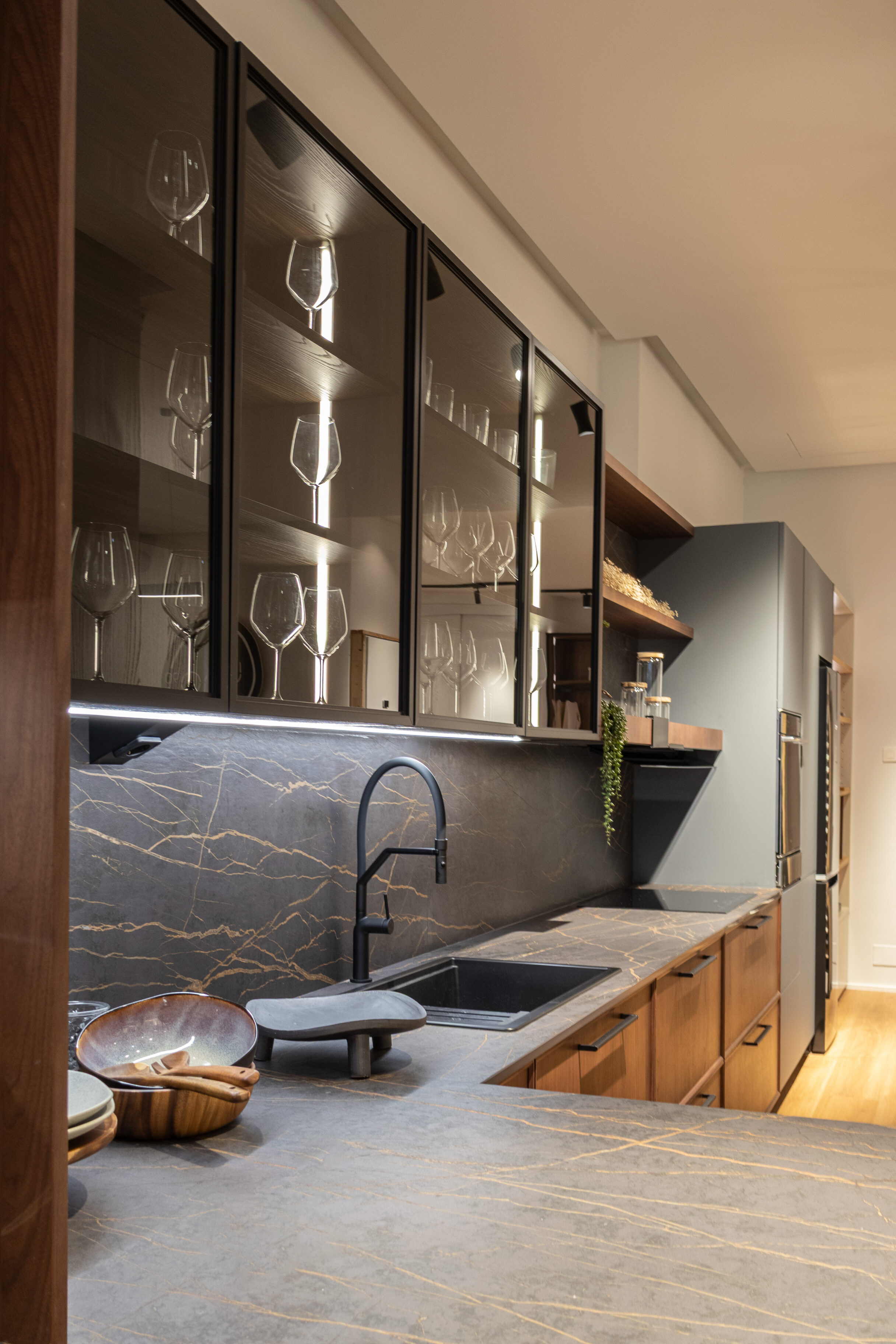 Cocina moderna con encimera de piedra natural, fregadero negro y cristales en estantes